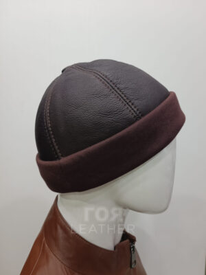 АРТИКУЛ: D- 02 | ЦВЯТ: Кафяв Кожена шапка модел Докер комбинира гладка горна част от агнешка тула и широк плетен маншет за изчистен, съвременен вид. Меката кожена горна част среща текстилния маншет, което дава балансиран микс от текстура и комфорт. Кожена изработка: Истинска агнешка кожа-тула с покритие образува здрав външен слой, който запазва формата си при ежедневно носене. Комфортна форма: Текстилния маншет и меката кожа осигуряват плътно и удобно прилягане, което се усеща леко на главата. За всекидневно носене: Универсален профил и гъвкави материали правят шапката лесна за носене и комбиниране с връхни дрехи. Практичния кафяв цвят подхожда както на ежедневни, така и на по-елегантни визии и върви добре с дънки, палта и плетива. Контрастът между кожа и плетиво прави визията по-интересна, като запазва сдържан вид.